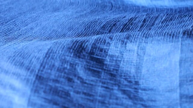 Blue natural silk fabric blowing in the wind and creating abstract waves. Soft textile material with geometric check pattern moving and rippling. Elegant flowing silk background with smooth motion.