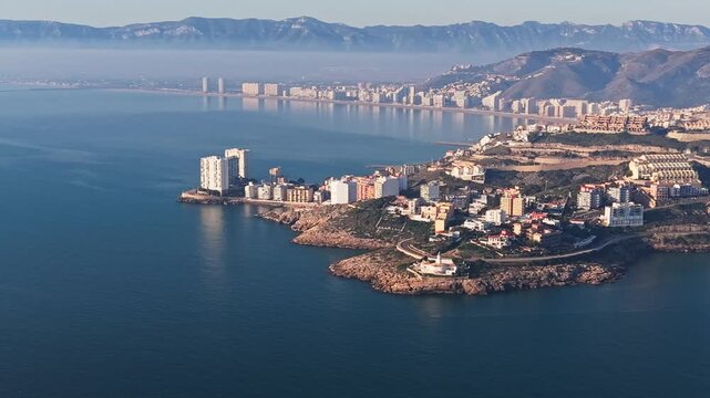 Aerial video frame of the El Faro district in Cullera with rocky peninsula, seafront buildings and Mediterranean bay, Spain