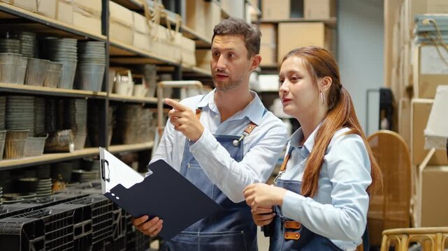 Professional male and female caucasian warehouse manager wearing aprons inspect inventory and check stock levels using a clipboard and barcode scanner in a large storage facility or local retail shop.