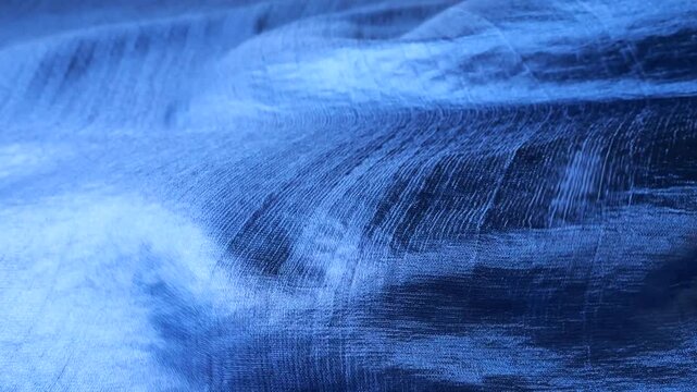 Blue natural silk fabric blowing in the wind and creating abstract waves. Soft textile material with geometric check pattern moving and rippling. Elegant flowing silk background with smooth motion.