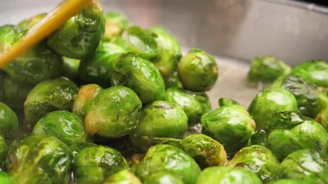 Slow motion. Frying juicy fresh green Brussels sprouts in a frying pan with vegetable oil. Shiny sparkling Brussels sprouts shoots. Vegetarian hot dish. Vegetable food. Not frozen food.