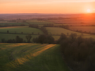 Fototapeta premium Aerial view of rolling green fields and hedgerows at sunset