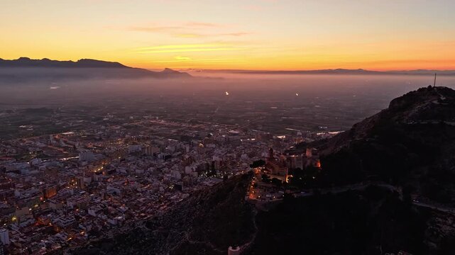 Aerial timelapse video frame of Cullera Castle above the city with mountain silhouettes and morning haze, Valencia, Spain