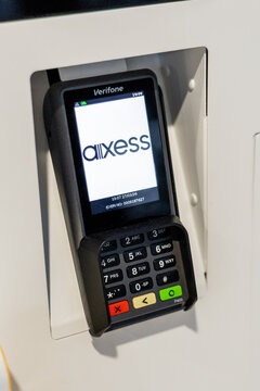 A close-up of a payment Verifone P400 Plus terminal mounted on a wall. The terminal displays a logo Axess and has a keypad with various buttons for transactions.