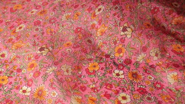 Abstract pink floral silk fabric fluttering in the wind. Natural silk material with vintage flower pattern creating soft waves. Seamless flow of textile with orange and white botanical print.