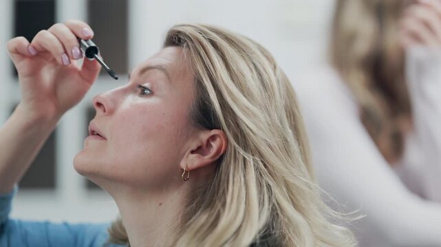 Blonde woman applying mascara to eyelashes