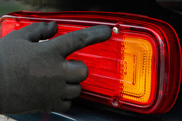 Hand in glove pointing at tail light screw © Aliaksandr