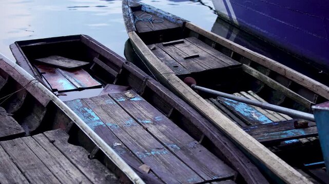 Panning across three weathered wooden fishing boats taking on water, tightly moored together at the edge of Selorejo Reservoir, Indonesia, showing the decay and neglect of traditional transport.