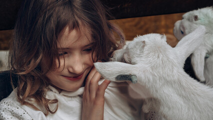 Child bonding with baby goats in a warm rustic barn © Anna