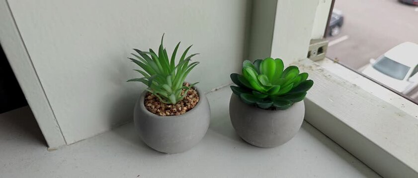 Two small artificial succulent plants in grey pots on a windowsill.