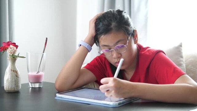 Close-up of a focused young girl wearing glasses using a digital tablet and stylus for online learning or homework at home, modern education and technology concept.