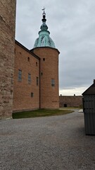 Exterior view of a tower at Kalmar Castle featuring ochre stone walls, historic windows and a gravel courtyard beneath an overcast sky. © Pim