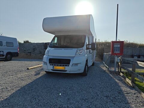 Motorhome parked at a campsite connected to an electricity hook-up under bright sunlight, representing travel, road trip lifestyle and outdoor living.
