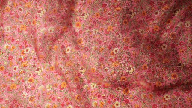 Flowing natural silk fabric with small floral pattern waving in the wind. Abstract background of soft waves and ripples in pink and orange tones. 