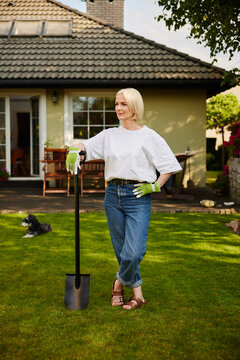 Woman resting on shovel in backyard garden on sunny day