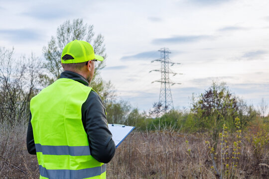 Rear view an electrical engineer or environmental auditor inspects power lines. The expert assesses the infrastructure's impact on the environment. Electrical grid maintenance and inspection.