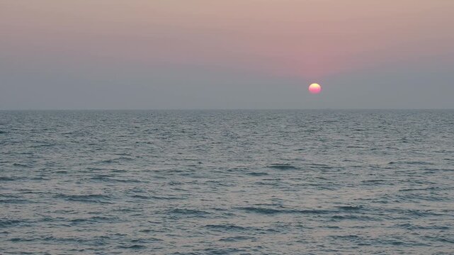 A calm ocean as the sun sets in a soft pastel sky.