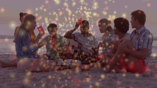Diverse friends sitting on sandy beach at sunset, playing guitar amid sparkles and raising red cups