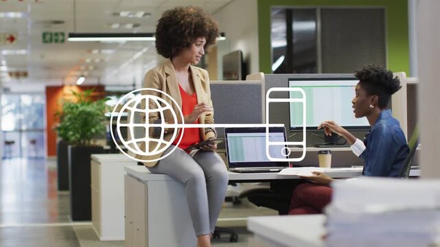 Left woman tapping tablet causing globe-phone overlay as right woman pointing sheet showing sales