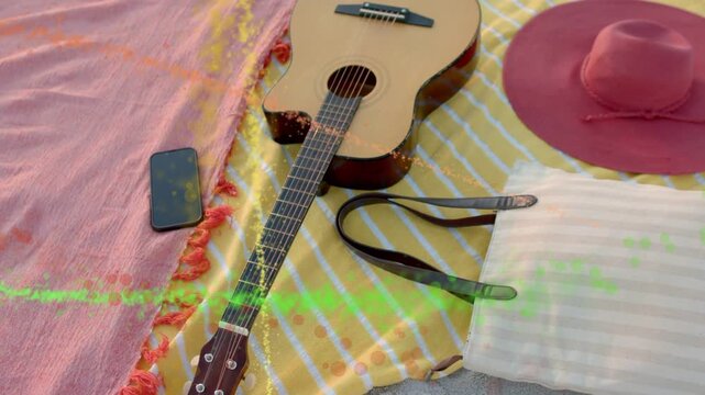Colorful streaks sweeping from left, revealing guitar, phone and hat, showcasing beach picnic