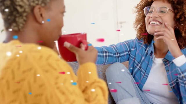 Vertical video: Women chatting on couch, one sipping red mug as other gesturing, marketing confetti