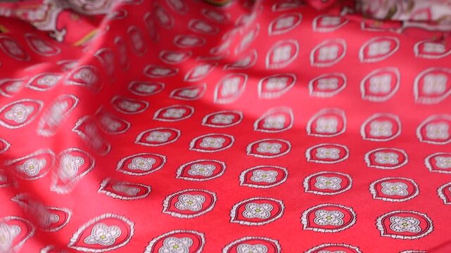 Natural silk fabric with abstract patterns waves in the wind. Red material creates a flowing background with geometric shapes. Soft ripples of real silk moving outdoors. Elegant textile texture.