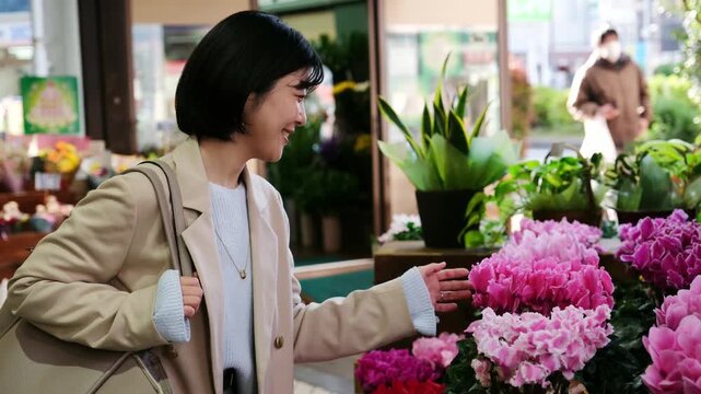 Smiling asian woman choosing a beautiful bouquet of pink flowers at a street flower market in Japan
