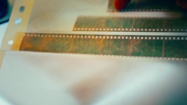 Analog film negatives selection finger photography archive closeup. Vintage strip evaluation light table detail macro frame sequence review process