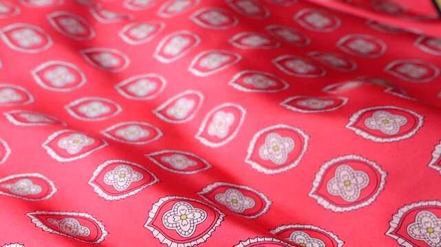 Red natural silk fabric with abstract oriental pattern develops in the wind. Soft waves of luxury textile create a flowing background. Elegant pink material with geometric ornaments.