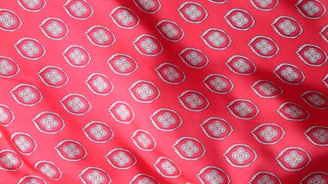 Red natural silk fabric with abstract oriental pattern develops in the wind. Soft waves of luxury textile create a flowing background. Elegant pink material with geometric ornaments.
