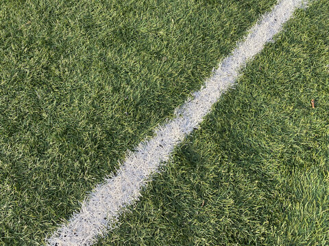 Close up of line on football or soccer pitch. Professional artificial grass surface with sports field line marking. White boundary line on green artificial grass of sports field. Synthetic turf