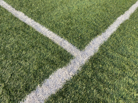 Artificial grass surface with sports field line marking. Football or soccer pitch. White boundary lines on green artificial grass of sports field. White painted markings on synthetic turf