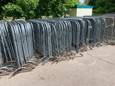 Control barriers. Steel pedestrian barricades lined up on asphalt near green park trees. Grey portable fencing for event security and temporary border management.