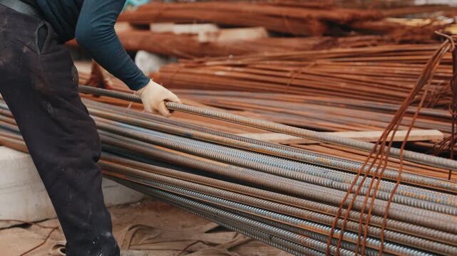 Worker handling steel rebar rods at construction site