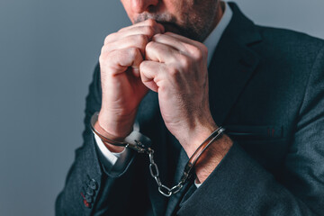 Handcuffed businessman with clenched hands, representing arrest, justice, financial crime, investigation, and loss of freedom in professional life. © Bits and Splits