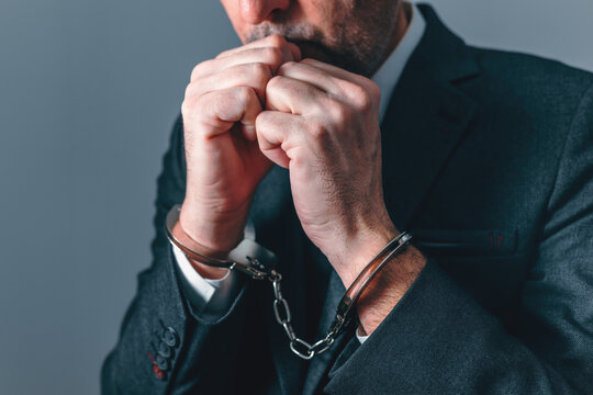 Handcuffed businessman with clenched hands, representing arrest, justice, financial crime, investigation, and loss of freedom in professional life.