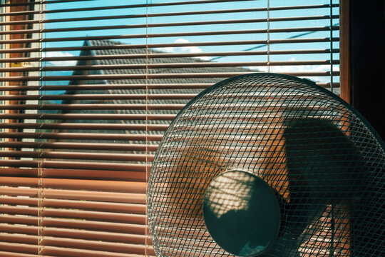 Electric fan in a room by a window with aluminum blinds on a hot summer day.