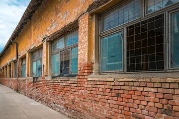 Fototapeten Gebäude In Trümmer Old abandoned factory building with red brick base and yellow peeling facade  © Bits and Splits