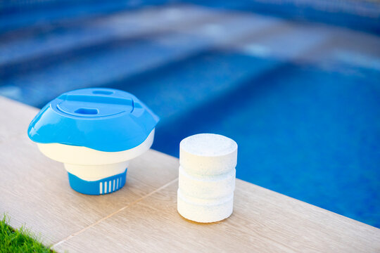 Plastic chlorine floater and stacked tablets on the edge of a swimming pool - pool maintenance concept