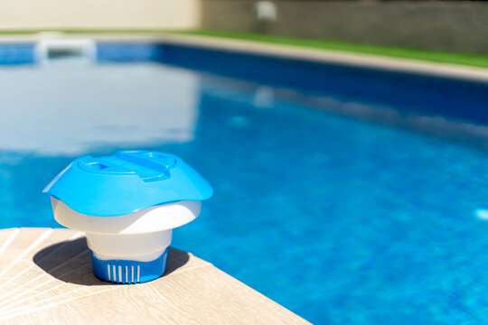 Plastic floating chlorine dispenser resting on pool edge with clear blue water in background - pool maintenance concept