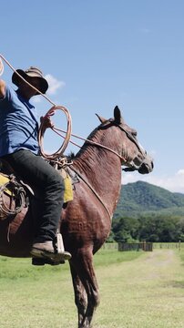 Skillful latino cowboy on horseback practicing his roping technique in a green field. The man expertly swings the lasso over his head