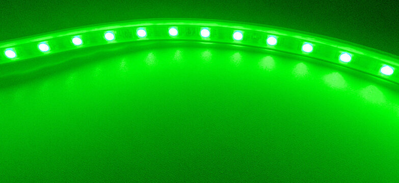 Glowing green led light strip background with neon illumination, abstract luminous technology backdrop, flexible led ribbon lighting, modern bright copy space