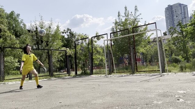 Teen boy practicing football juggling with knee on outdoor court focused training of ball control coordination and technique youth sport concept. High quality FullHD footage