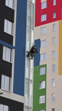 Industrial mountaineering man worker applying washing foam on glazing using microfiber sponge. Male rope access laborer in work uniform during high-rise job. Industry urban works concept.