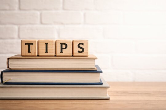 TIPS spelled on wooden cubes placed on books against a white brick wall featuring blank copy space