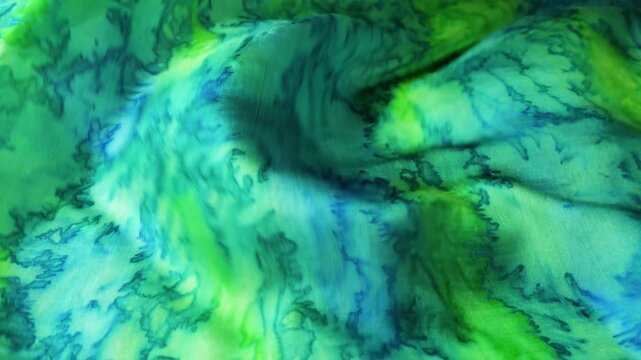 Silk fabric waving in the wind. Abstract green and blue wavy background. Flowing textile with marble pattern. Soft silk material fluttering in slow motion.