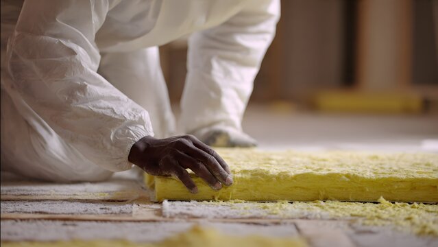 Hands positioning thick yellow insulation between wooden floor joists, 4K