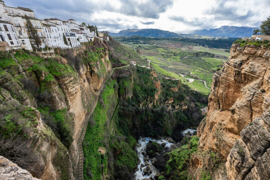 Scenic view looking down into the lush green El Tajo gorge in Ronda, showing the river and the dramatic limestone cliffs from above.