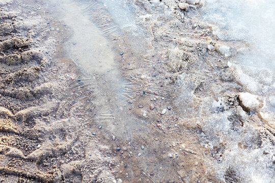 Winter road surface details. Closeup of icy mud with saline deposits and melt patterns