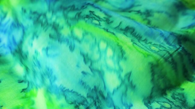 Abstract green and blue waves of natural silk fabric fluttering in the wind. Soft textile background with emerald and turquoise colored patterns. Beautiful ripples of silky cloth creates fluid motion.